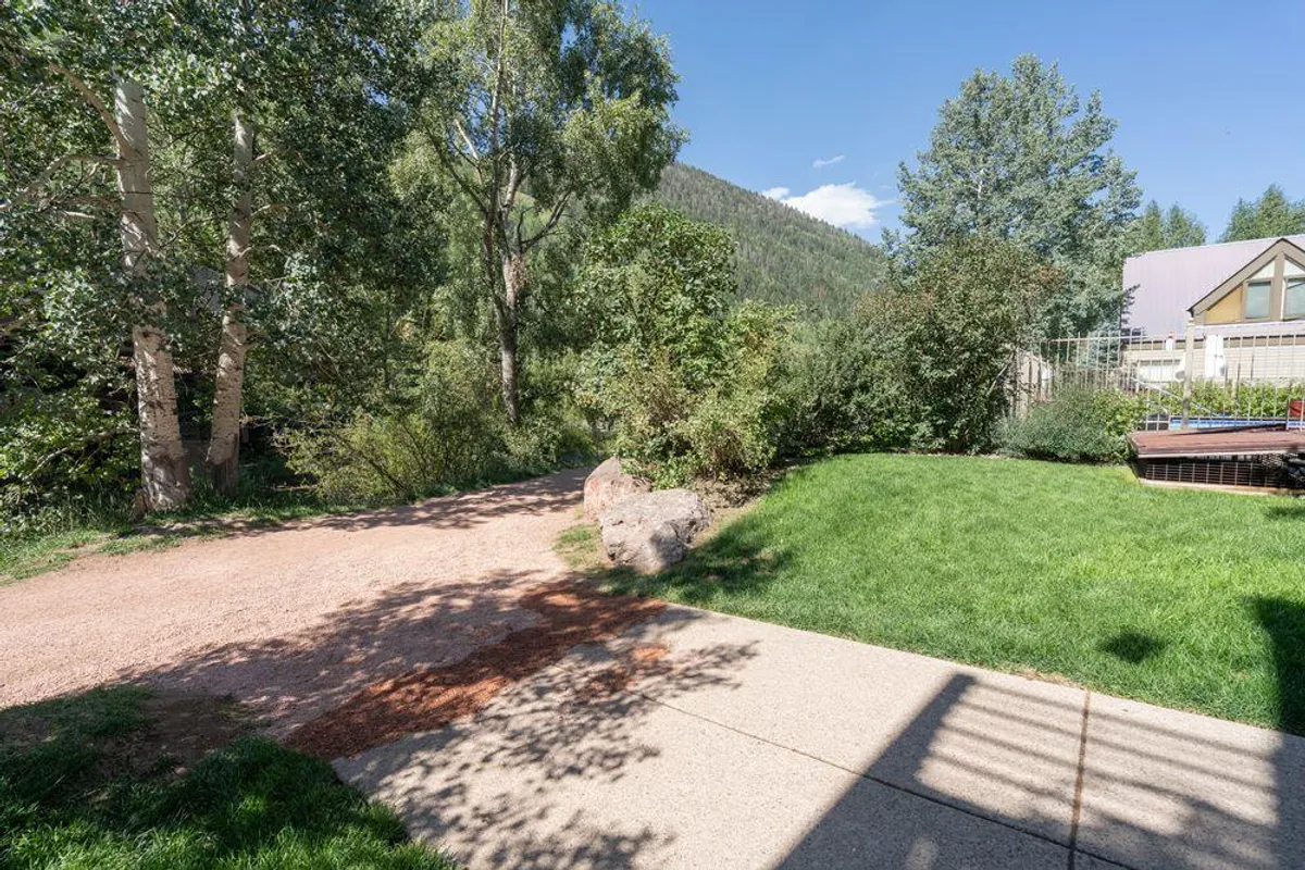 A tranquil gravel path bordered by lush greenery leads toward dramatic mountain views, bathed in beautiful sunset light. The setting evokes a sense of peaceful seclusion and natural romance, perfect for morning strolls with coffee or evening walks as a couple.