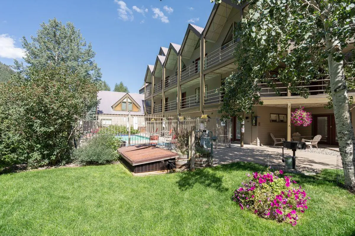 This image showcases a well-maintained swimming pool surrounded by vibrant flower beds and outdoor seating, with the building's facade visible in the background. The area exudes a sense of relaxation and is clearly designed for social gatherings and enjoyment under the sun.