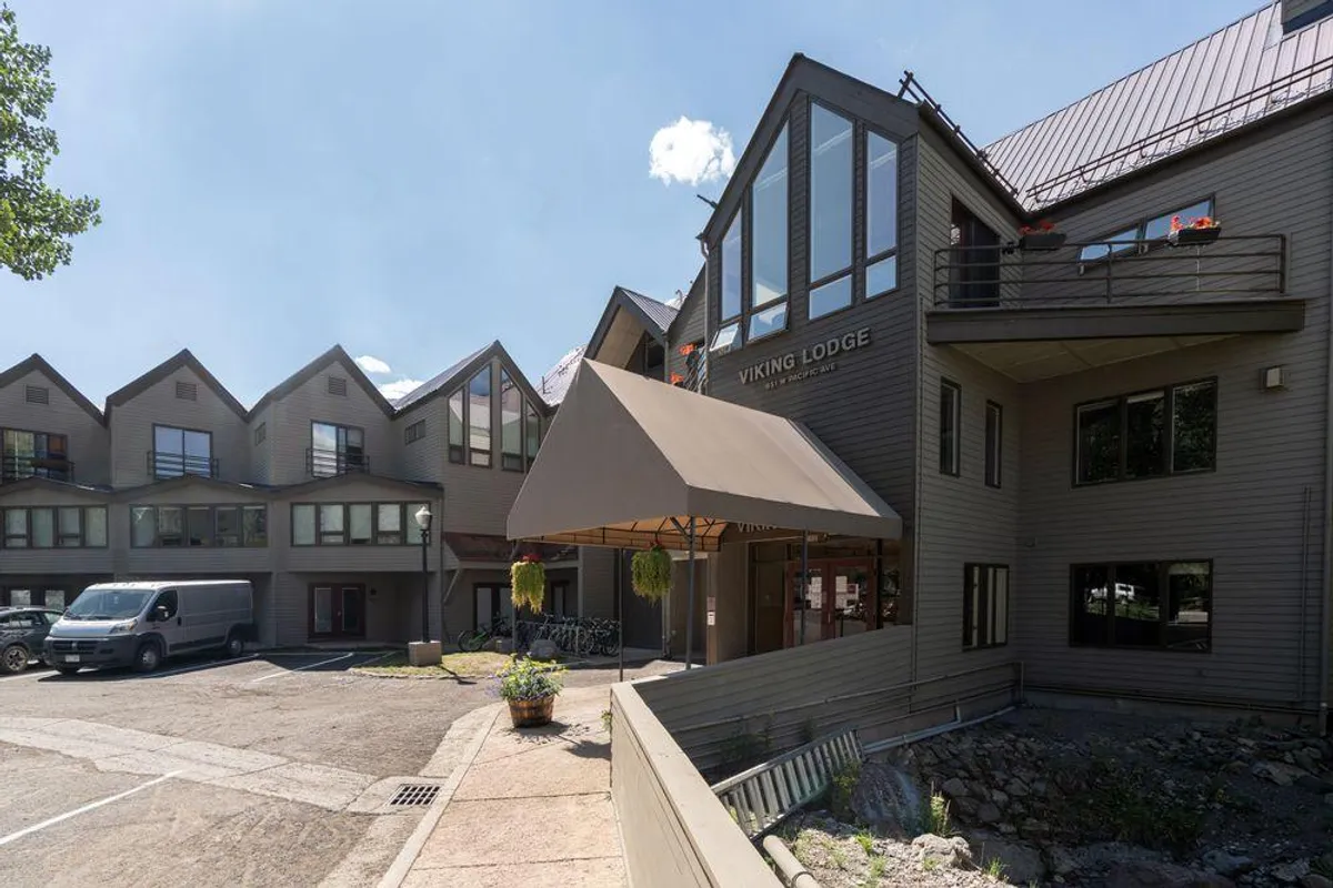 A welcoming exterior shot of Viking Lodge with its inviting entrance awning, large windows, and tasteful landscaping. The patio is visible, offering a spot to relax and take in the surrounding mountain scenery. The ambiance is cozy and inviting, hinting at the ease of stepping right outside to explore Telluride's dining and nightlife.