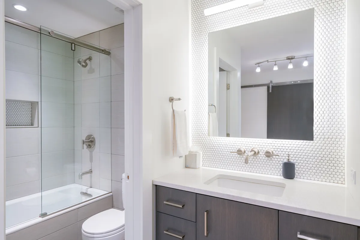 A stylish bathroom with a glass shower enclosure, hexagonal tile backsplash, and a modern sink and faucet. The space is well-lit and spotlessly clean, highlighting a fresh and inviting ambiance.