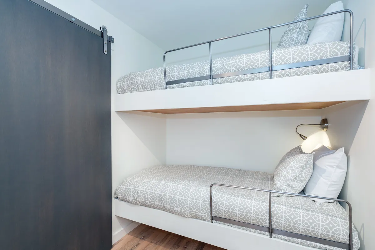 A detailed shot of cozy bunk beds with textured bedding, soft lighting from a wall-mounted fixture, and a welcoming, playful atmosphere. The arrangement suggests a comfortable spot for reading, resting, or telling bedtime stories.