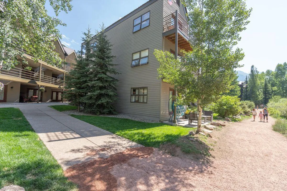 This image features the exterior façade of Viking Lodge, with surrounding greenery and a welcoming pathway that leads away from the property. Guests can be seen walking along the path, enjoying the natural setting, and socializing on the balcony. The scene exudes a relaxed, inviting atmosphere.