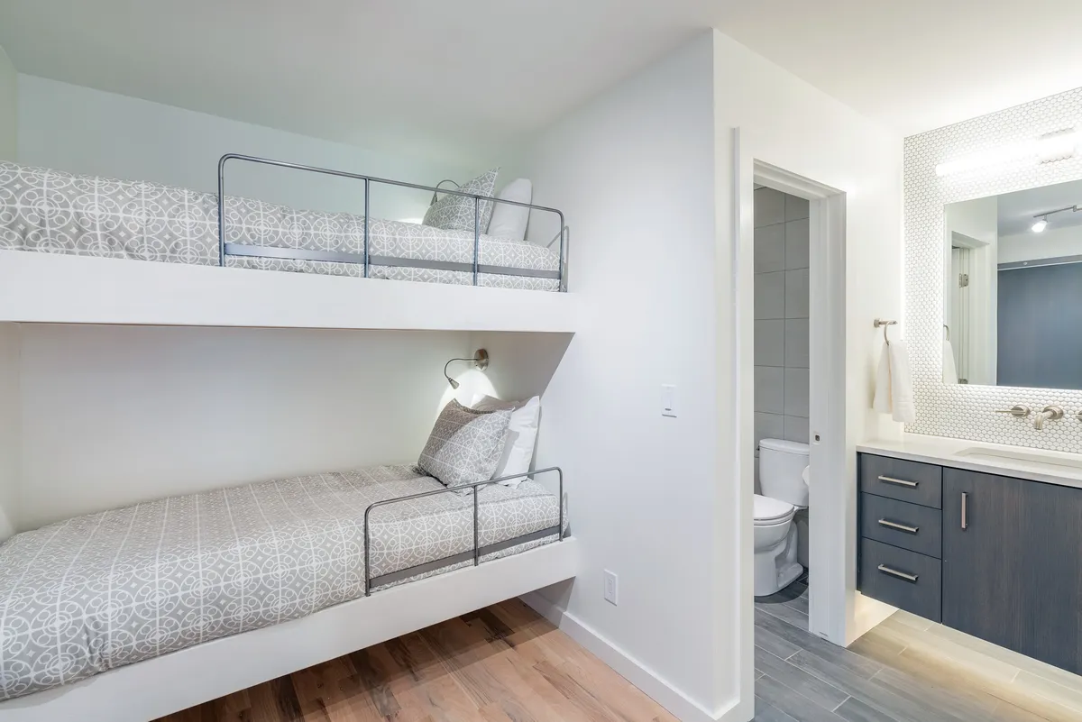 A close-up view of the bunk nook, highlighting two bunk beds with neat bedding, a small vanity area, and the nearby bathroom door. The scene feels both practical and cozy, perfect for young explorers and family routines.
