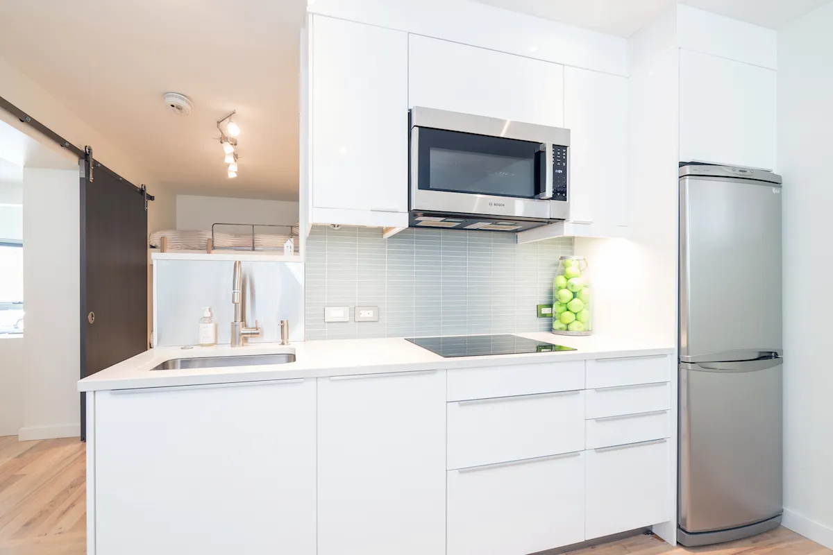 A bright, modern kitchen featuring sleek cabinetry, stainless steel appliances, and a pop of color with a green apple decoration on the countertop. The space is organized, clean, and inviting, suggesting both high standards of cleanliness and thoughtful design.